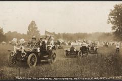 A parade of Model T type cars driving across a field