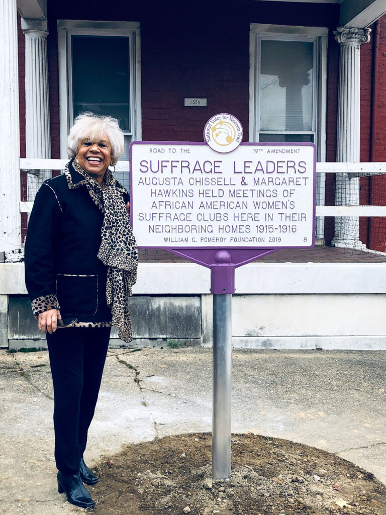 Carolyn Chissell stands next to a historic marker celebrating Augusta Chissell and Margaret Hawkins.