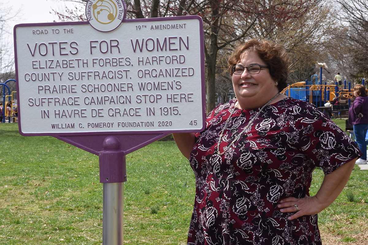 Maria Darby, MWHC Board President, stands next to marker