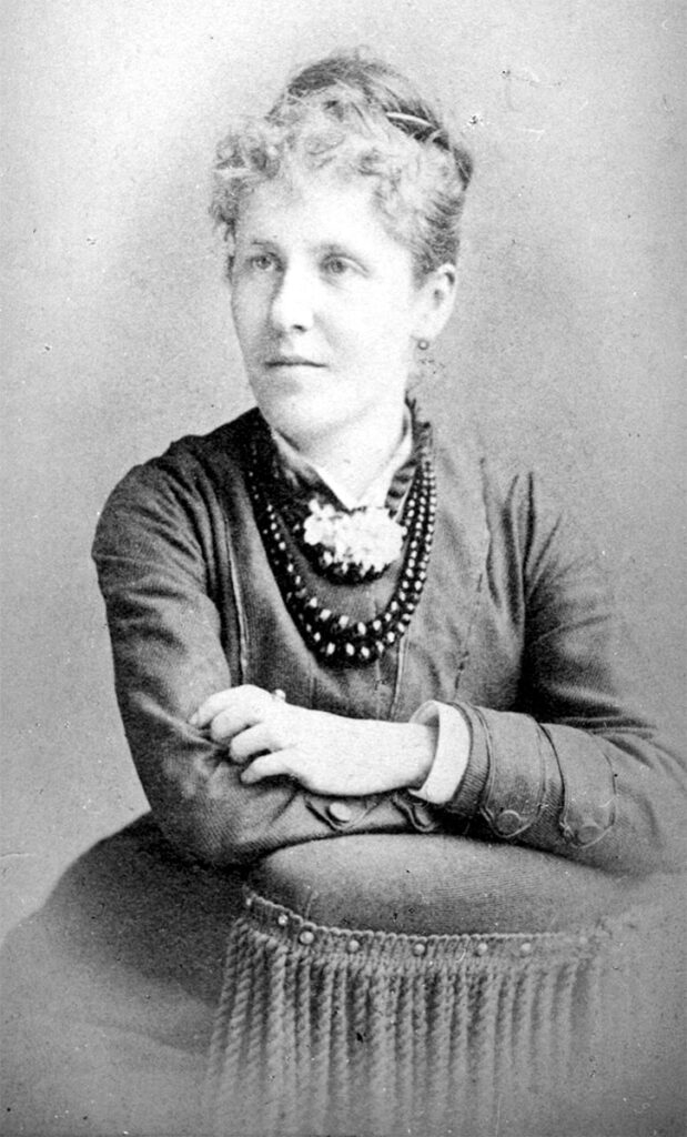 Black and white studio photo of Mary Shellman. She is leaning on a platform and looking to her right. Wearing a suit and set of large beaded necklace