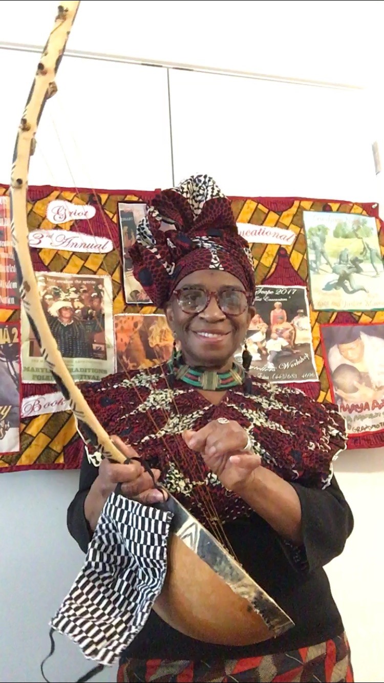 Griot Grandmother Edna in African American inspired dress, hiding a wooden string instrument