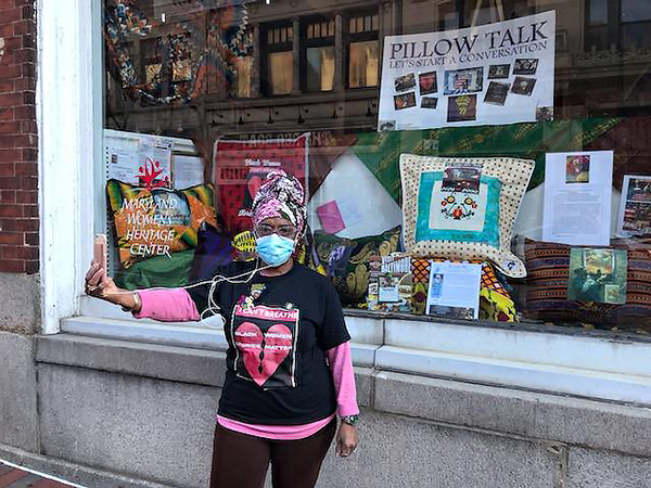 Grandmother Griot Edna standing outside in front of the display window that holds her African American inspired quilts