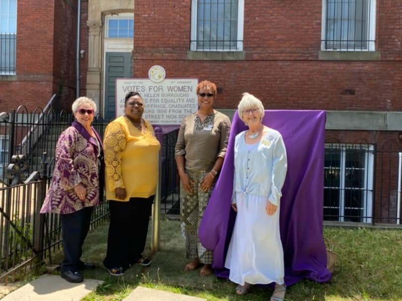 Four women standing in front of a suffrage marker in honor of Nannie Helen Burroughs