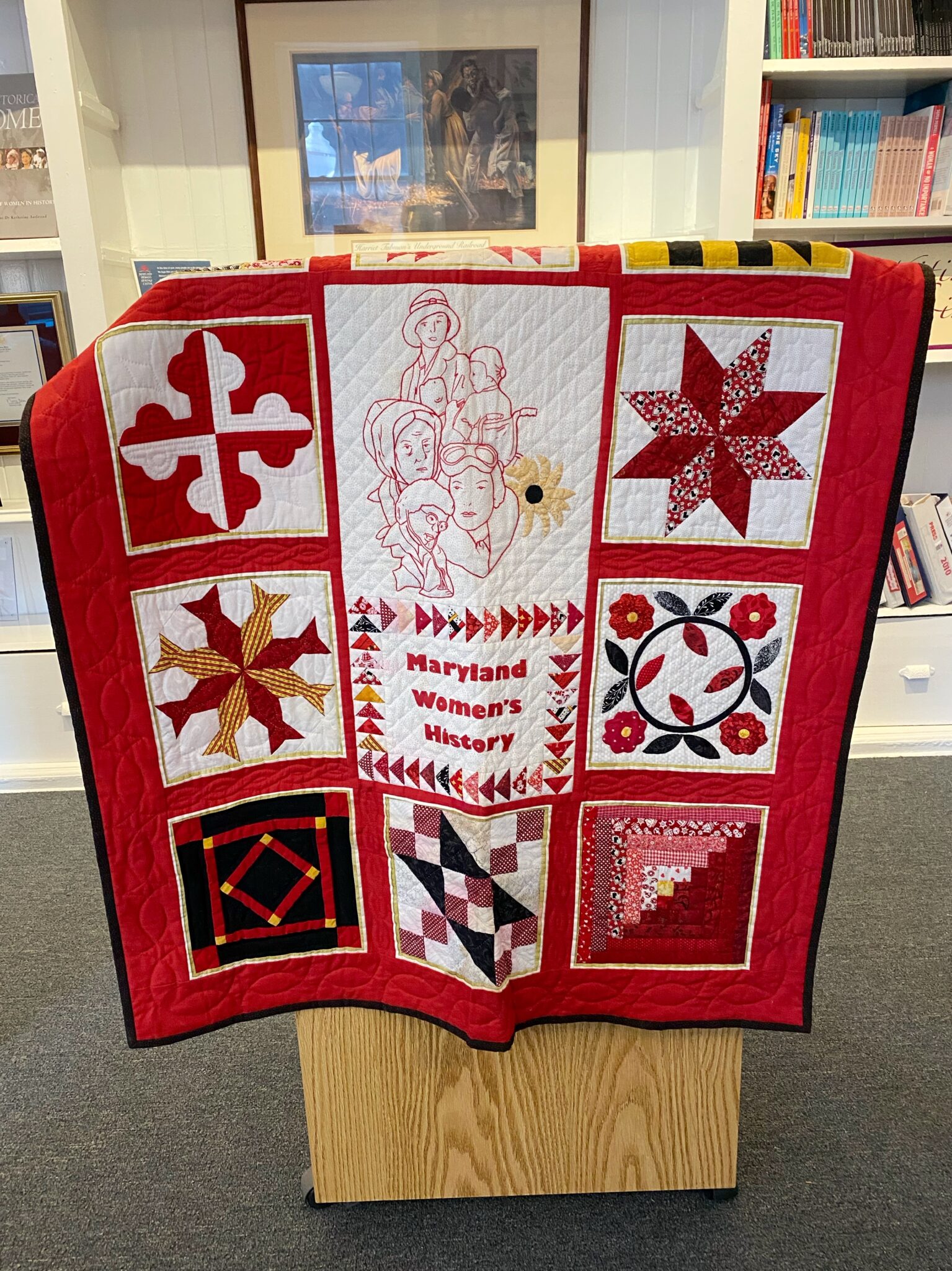A red, black and white quilt with a center square that says "Maryland Women's Heritage Center."