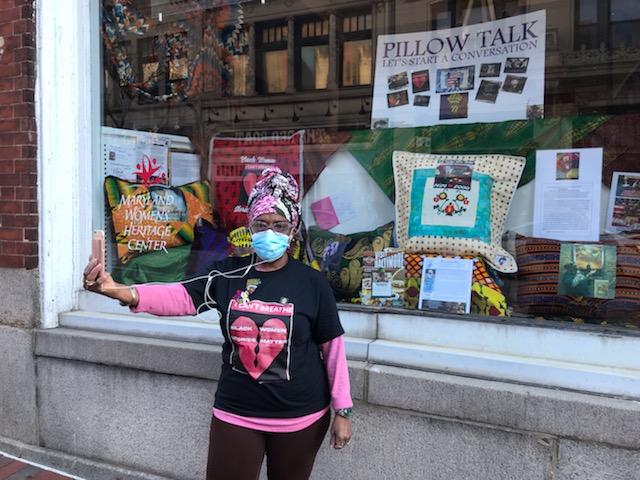 Edna Williams, wearing a mask, stands in front of her quilt exhibition