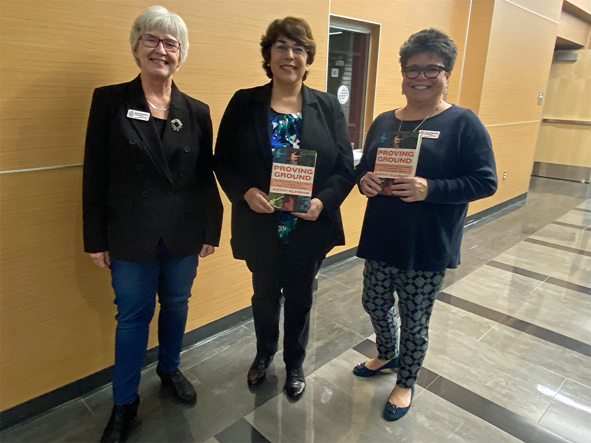 three women, two holding the book called "Proving Ground"