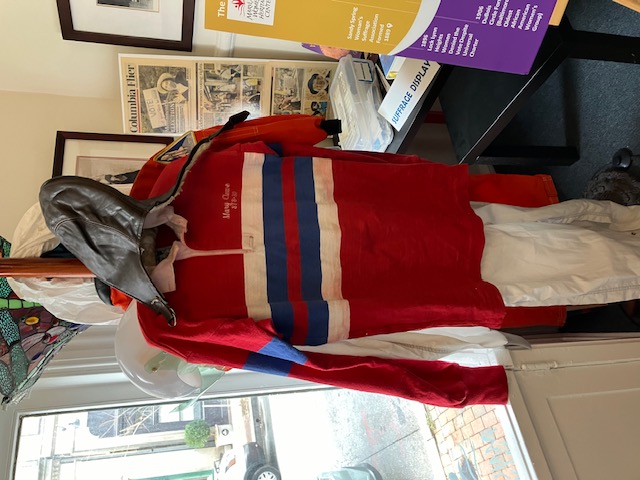 A NASA work uniform on a pedestal. It is a red polo shirt with blue and white stripes and belonged to Mary Cleave 