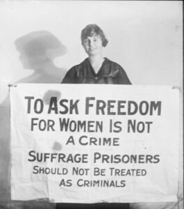 A woman circa 1900s holding a sign that says To ask for freedom for women is not a crime