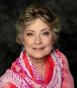 Kate Stevenson looking into camera from side pose, wearing pink and red colors