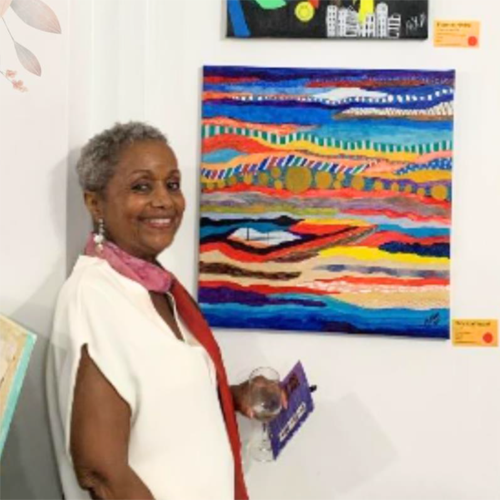 Malynda Madzel wearing a white dress stands in front of an abstract painting and smiles over her shoulder