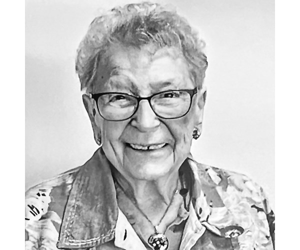 A Black and white headshot of Joanne Goldsmith. She has short gray hair and is wearing glasses and a print jacket