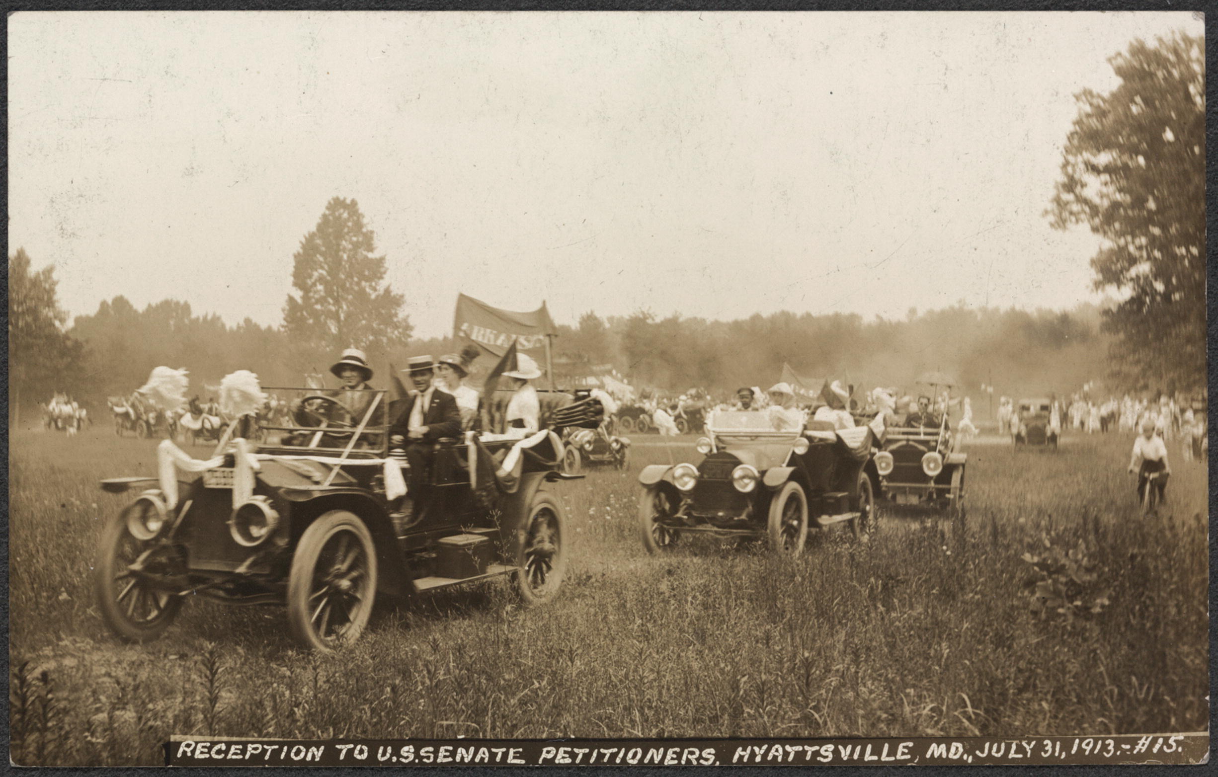 A sepia photograph of suffragists driving across a field in 1920s era autos