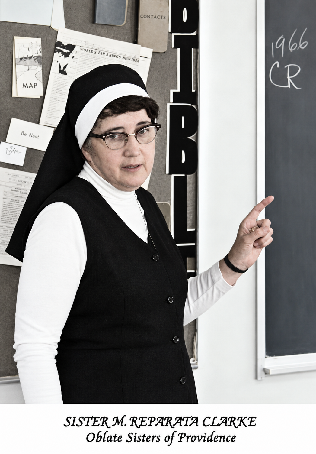 Sister Reparata in contemporary nun hair pointing to black board and looking at camera