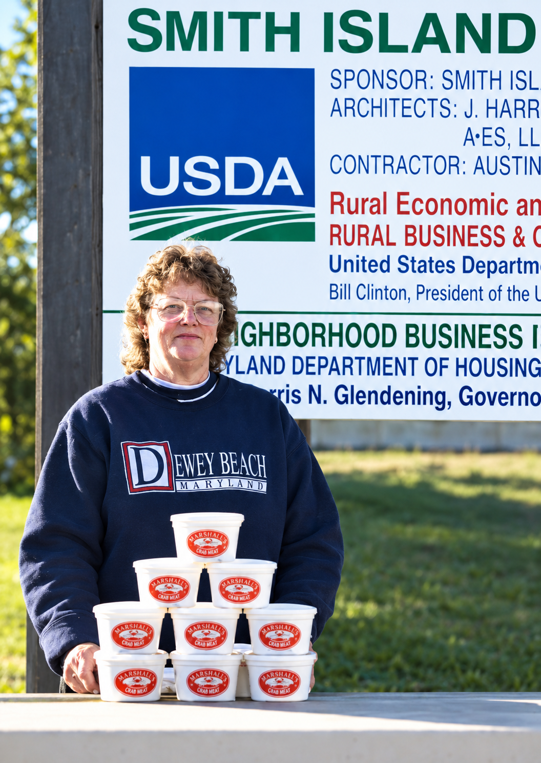 image of Janice Marshall in front of a sign Smith Island. She is holding containers of crabmeat